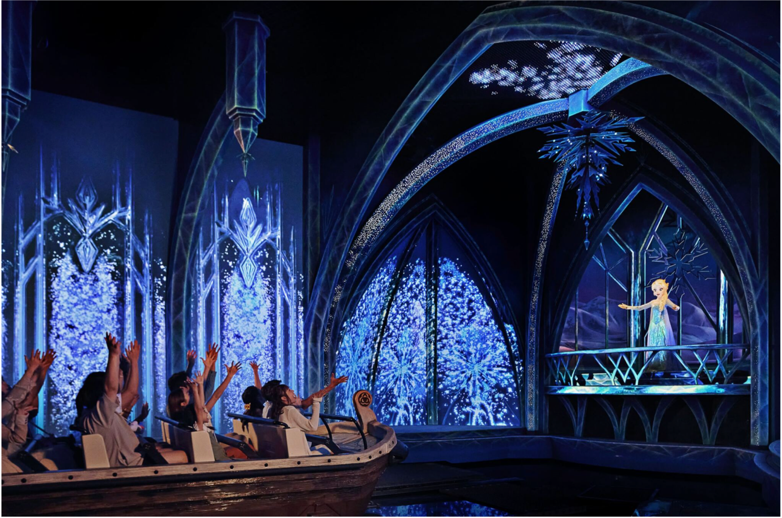 Boat filled with guests sailing past Elsa performing in her Ice Palace with projections and snow effects.